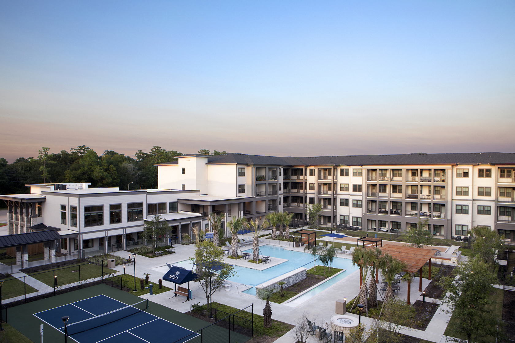 an aerial view of a resort-style pool and courtyard, pickleball court, and patio area at a senior apartment community